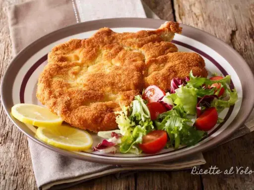Cotoletta alla milanese dorata e croccante, servita con insalata fresca e spicchi di limone.