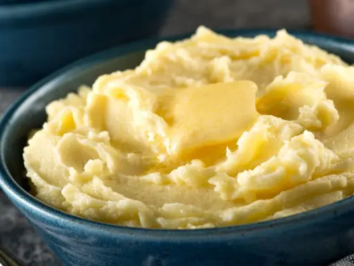 Una ciotola blu piena di soffice purea di patate, con una fetta di burro che si scioglie sopra.