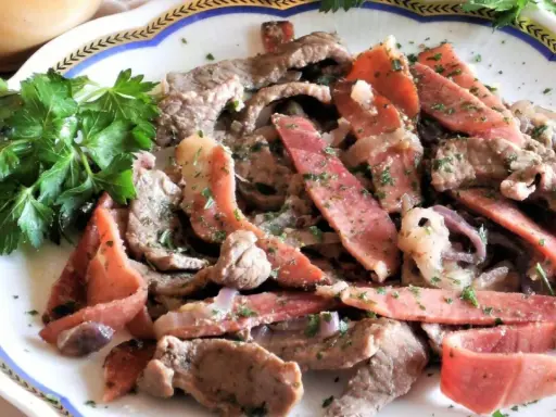 Straccetti di manzo con pancetta e cipolla, guarniti con prezzemolo fresco. Un piatto saporito e invitante.