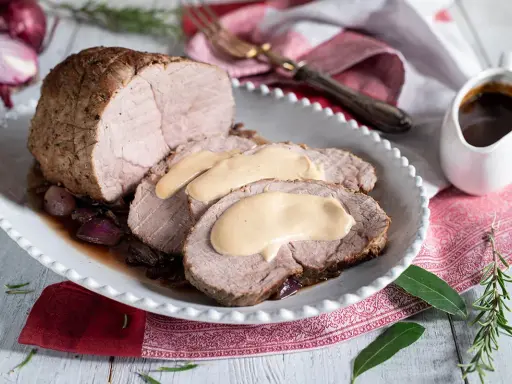 Arrosto di vitello morbido con sughetto benedetta, servito su un piatto bianco con cipolle rosse caramellate e rosmarino.