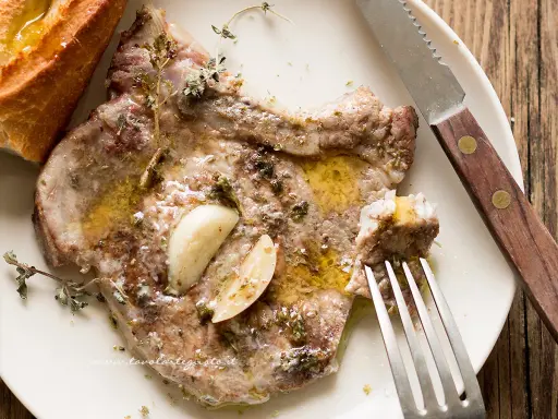 Braciola di maiale succulenta, condita con aglio e erbe aromatiche, servita con pane croccante.
