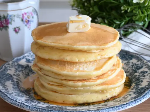 Pila di soffici pancake con farina di avena, guarniti con burro e sciroppo d'acero, su un piatto decorato.