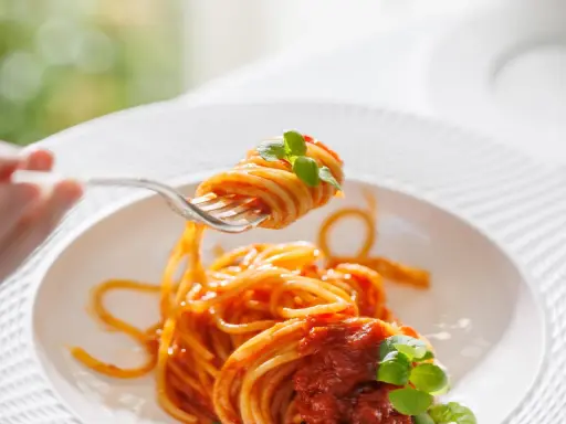 Un primo piatto invitante: spaghetti al dente conditi con un sugo rosso vivo di pomodorini freschi e basilico, pronti per essere gustati.
