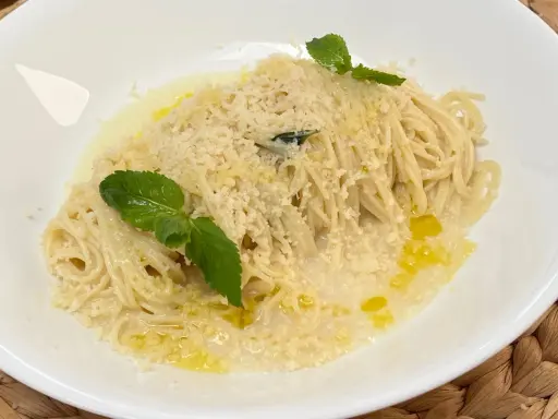 Spaghetti al limone cremosi, cosparsi di parmigiano e guarniti con foglie di menta fresca.