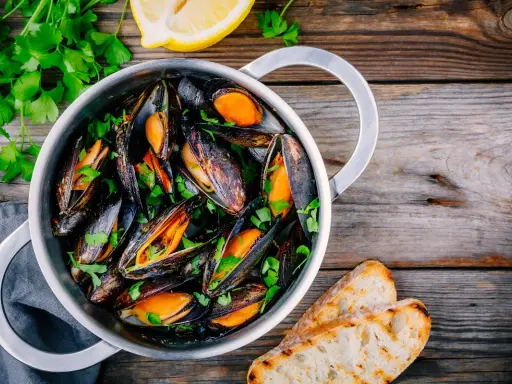 Un pentolino di cozze alla marinara, guarnite con prezzemolo fresco e accompagnate da fette di pane tostato e spicchi di limone.