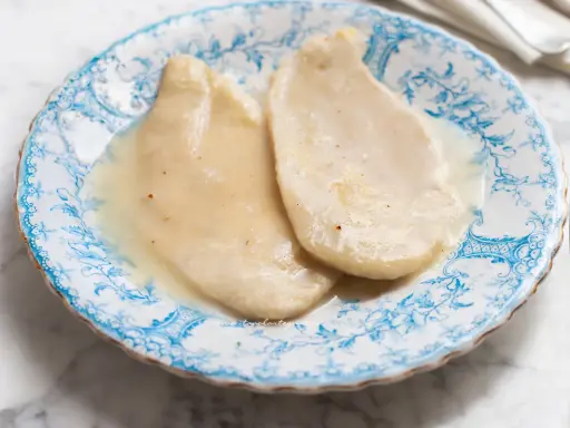 Due scaloppine al vino bianco, tenere e succulente, servite su un piatto decorato con motivi blu.