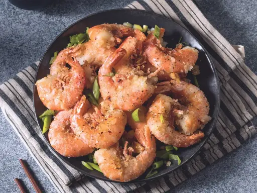 Gamberi sale e pepe croccanti, serviti su un piatto scuro con erba cipollina fresca. Un piatto invitante e saporito.