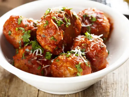 Polpette di carne morbide in salsa rossa, cosparse di parmigiano e prezzemolo fresco.