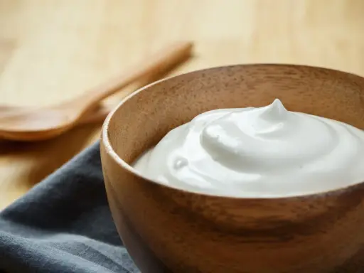 Una ciotola di legno piena di soffice crema al latte, pronta per essere gustata con due cucchiai in legno sullo sfondo.