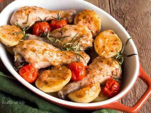 Delizioso pollo al forno con patate e pomodorini, guarnito con rosmarino fresco. Un piatto invitante e saporito.