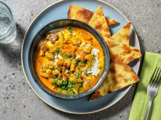 Un invitante pollo al curry cremoso, guarnito con coriandolo fresco e servito con pane naan croccante.