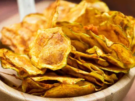 Croccanti chips di zucchine dorate, perfette per uno snack sano e gustoso, servite in una ciotola di legno.