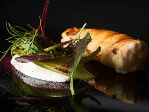 Spiedini di pesce avvolti in pasta sfoglia, serviti con una crema bianca e insalata fresca, su sfondo nero.