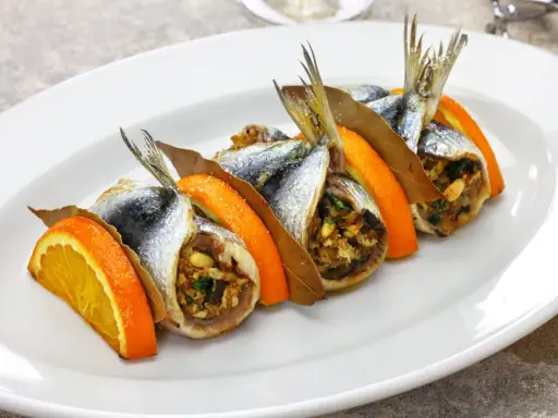 Sarde a beccafico, un piatto siciliano con sardine ripiene, arancia e alloro, servite su un piatto bianco.