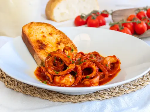 Moscardini in umido, teneri e saporiti, serviti con pane tostato e pomodorini freschi.