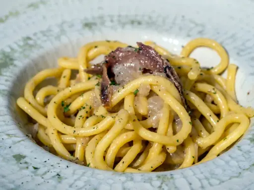 Un piatto di bigoli in salsa, pasta spessa condita con acciughe e cipolla, guarnita con prezzemolo tritato.