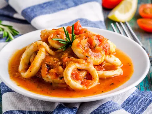 Calamari in umido succulenti, cotti in una salsa rossa saporita, guarniti con rosmarino fresco.
