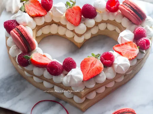 Deliziosa cream tart a forma di cuore per bambini, decorata con fragole, lamponi, meringhe e macarons.