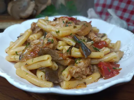 Un piatto invitante di pasta funghi e salsiccia, condita con pomodoro e prezzemolo, pronta per essere gustata.