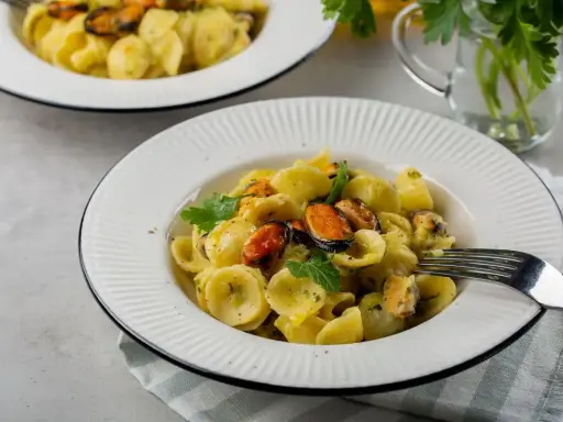 Orecchiette con patate e cozze, un piatto cremoso e saporito, guarnito con prezzemolo fresco.