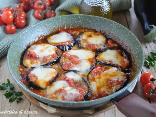 Melanzane alla pizzaiola in padella, con pomodoro e mozzarella filante, contornate da pomodorini freschi e basilico.