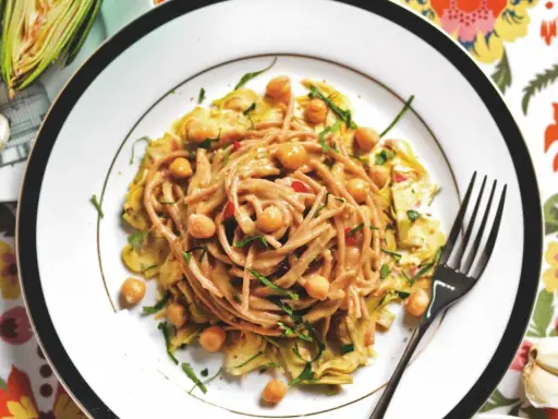 Un piatto invitante di pasta con carciofi alla siciliana, arricchito da ceci e erbe fresche, su un tovagliolo colorato.
