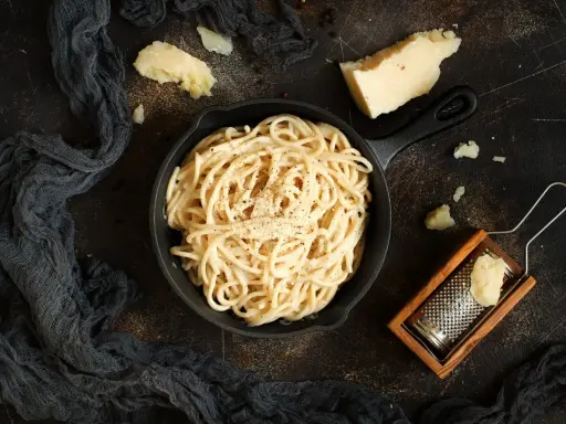 Un piatto di spaghetti cacio e pepe fumante, con pezzi di pecorino e una grattugia in legno.