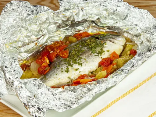 Orata al cartoccio con pomodorini e verdure, cotta al forno e servita in un foglio d'alluminio aperto.
