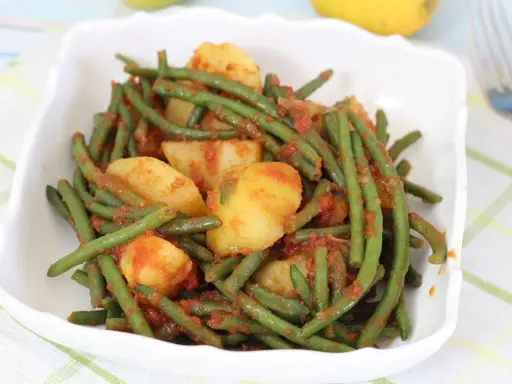 Un piatto di fagiolini in umido con patate, conditi con un sugo rosso saporito, servito in una ciotola bianca.