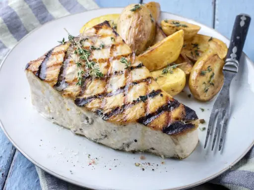 Un succulento trancio di pesce spada alla griglia, guarnito con timo fresco, servito con patate arrosto. Un'idea per le tue prossime ricette di pesce spada.