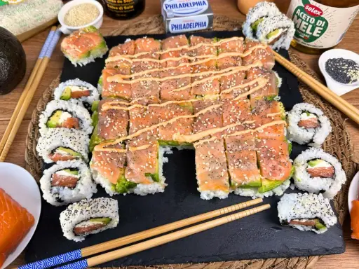 Un invitante sushi fatto in casa con salmone, avocado e formaggio Philadelphia, guarnito con semi di sesamo e una salsa cremosa.