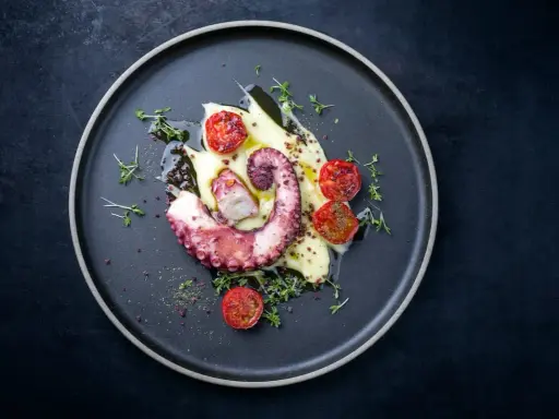 Un tentacolo di polpo alla griglia, servito su purè di patate con pomodorini confit e timo fresco.