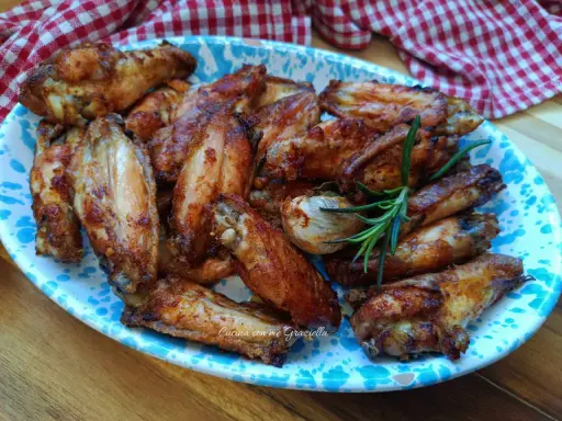 Alette di pollo dorate e croccanti, servite su un piatto decorato con un rametto di rosmarino.