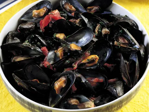 Una ciotola piena di saporita zuppa di cozze, con cozze nere aperte che rivelano la polpa succulenta, condita con erbe fresche e pomodoro.