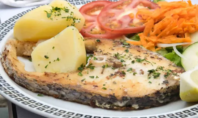 Un succulento pesce spada al forno, accompagnato da patate bollite, pomodori freschi, carote grattugiate e un'insalata leggera.