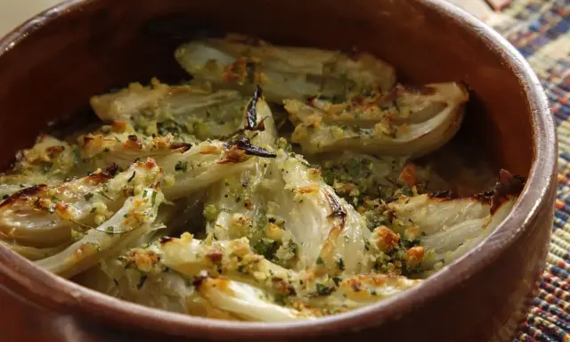 Finocchi al forno dorati e croccanti, conditi con erbe aromatiche e pangrattato, serviti in una terrina di terracotta.