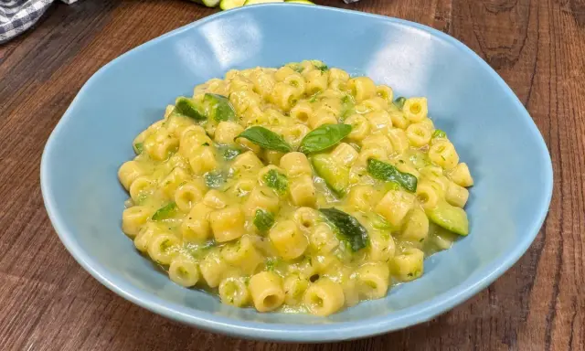 Un piatto di pasta con zucchine e basilico, cremoso e invitante, servito in una ciotola azzurra su un tavolo di legno.