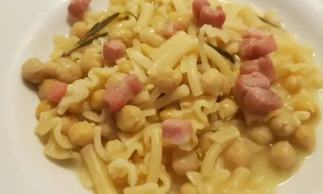 Piatto di pasta e ceci in scatola, con cubetti di pancetta e un rametto di rosmarino.