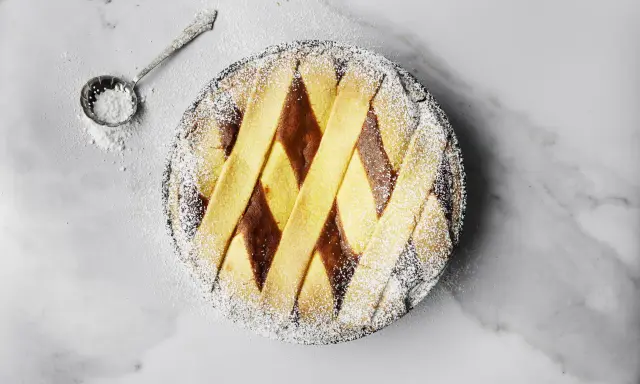 Pastiera napoletana pronta, cosparsa di zucchero a velo. Un cucchiaino d'argento è pronto per decorare, mostrando come si fa la pastiera.