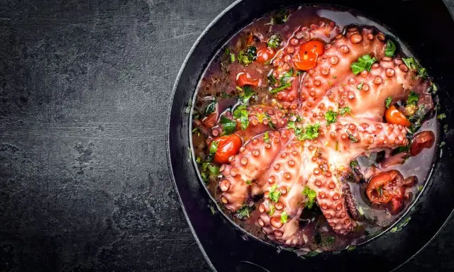 Polpo alla luciana in padella, con pomodorini e prezzemolo fresco. Un piatto succulento e profumato, pronto per essere gustato.