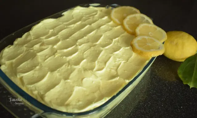 Un invitante tiramisù al limone, guarnito con fette di limone fresco e limoni interi, pronto per essere gustato.