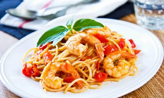 Spaghetti con gamberetti succulenti, pomodorini freschi e basilico, un piatto invitante pronto per essere gustato.