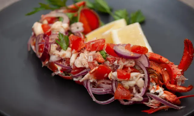 Astice alla catalana: un piatto fresco con astice, pomodoro, cipolla rossa e limone, guarnito con prezzemolo.