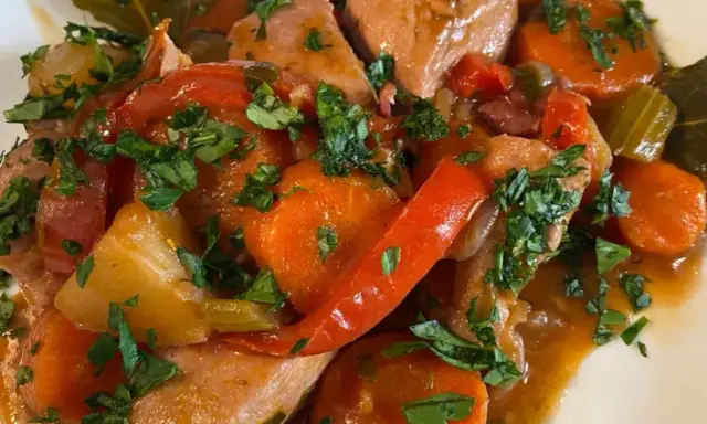 Un saporito spezzatino di pollo con carote, peperoni rossi e prezzemolo tritato, servito in un piatto bianco.
