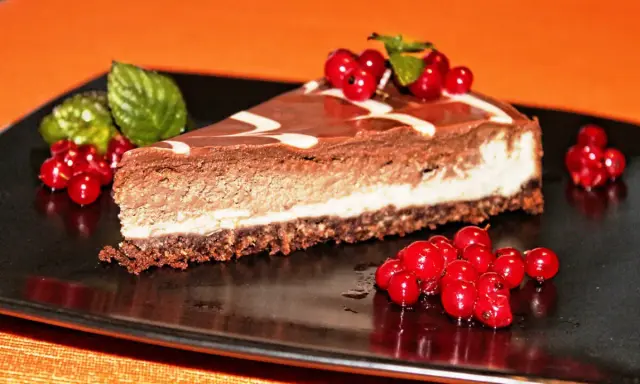Una fetta di cheesecake alla nutella, con glassa al cioccolato e decorata con ribes rossi e menta.