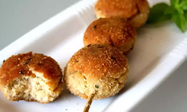 Polpette tonno e ricotta dorate su uno spiedino, una è stata morsa, con basilico fresco.