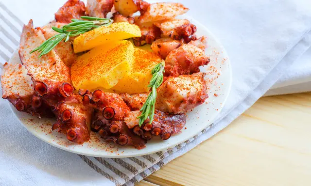 Un invitante polpo alla gallega, cosparso di paprika e guarnito con rosmarino e patate, pronto per essere gustato.