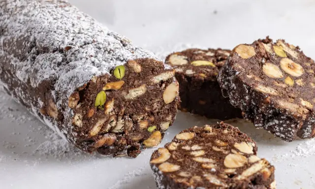 Salame di cioccolato senza uova, ricco di biscotti, nocciole e pistacchi, spolverato di zucchero a velo.