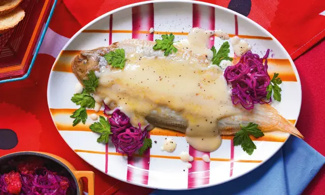 Sogliola alla mugnaia su piatto a righe, guarnita con cavolo rosso e prezzemolo.