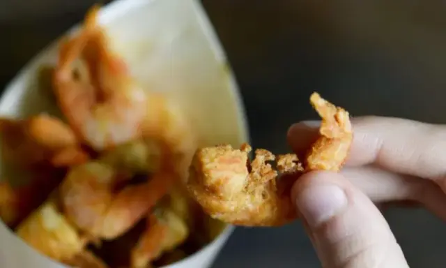 Una mano tiene un gambero croccante, parte di una deliziosa frittura di pesce servita in un cono di carta.